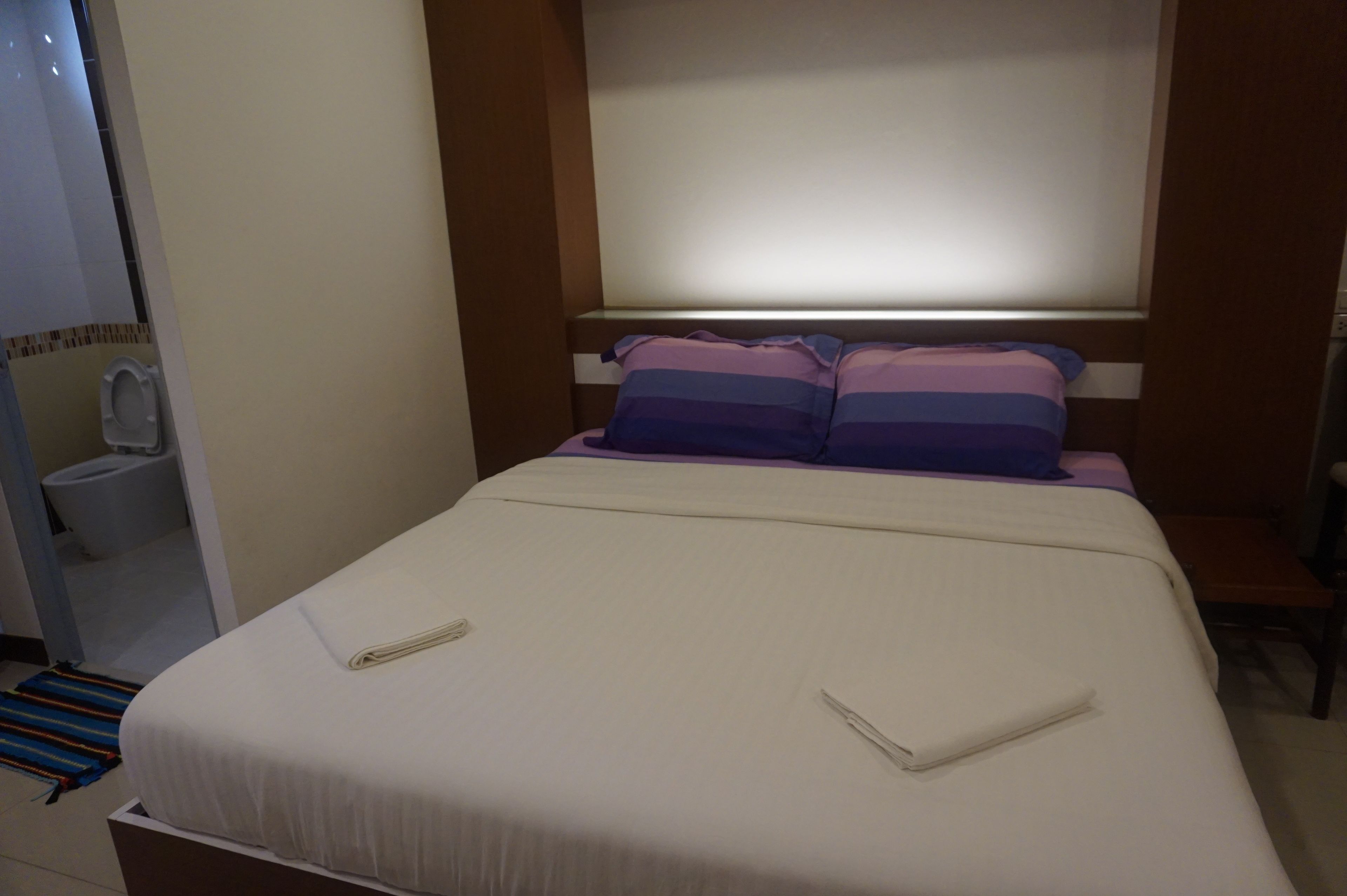 Habitación de hotel con cama, mesita de noche, persianas en la ventana y baño con inodoro y lavabo.