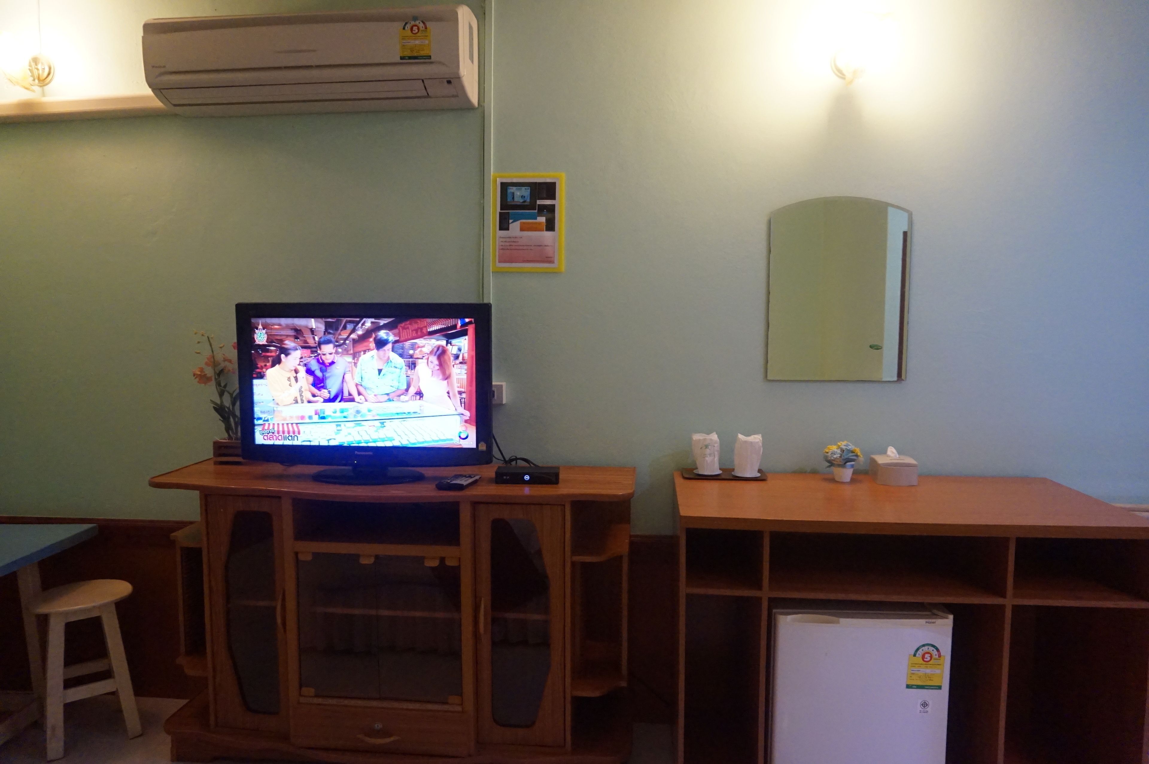 A room with a wooden TV stand holding a TV, a small refrigerator, and a mirror on the wall.