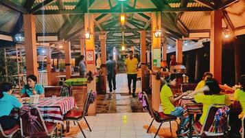 A restaurant with tables and chairs, a person walking, and a green light on the ceiling.
