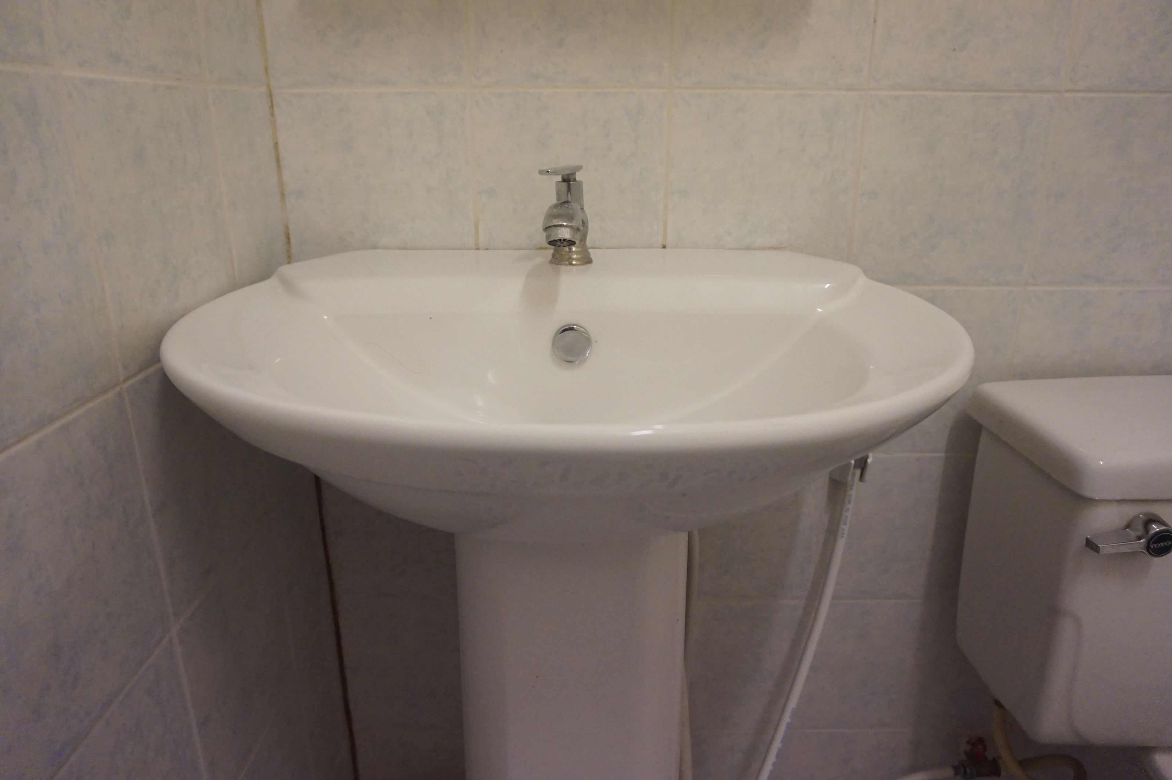 A bathroom with a white pedestal sink, a faucet, and a toilet.