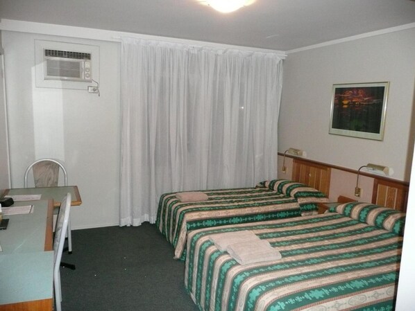 Een hotelkamer met twee eenpersoonsbedden, een bureau met stoel, een raam met gordijnen en een schilderij aan de muur.