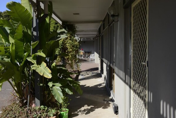 A narrow outdoor corridor with a covered walkway, potted plants, and a building entrance labeled "LA PUBLIC RESTAURANT". - The Hermitage Motel (Muswellbrook)
