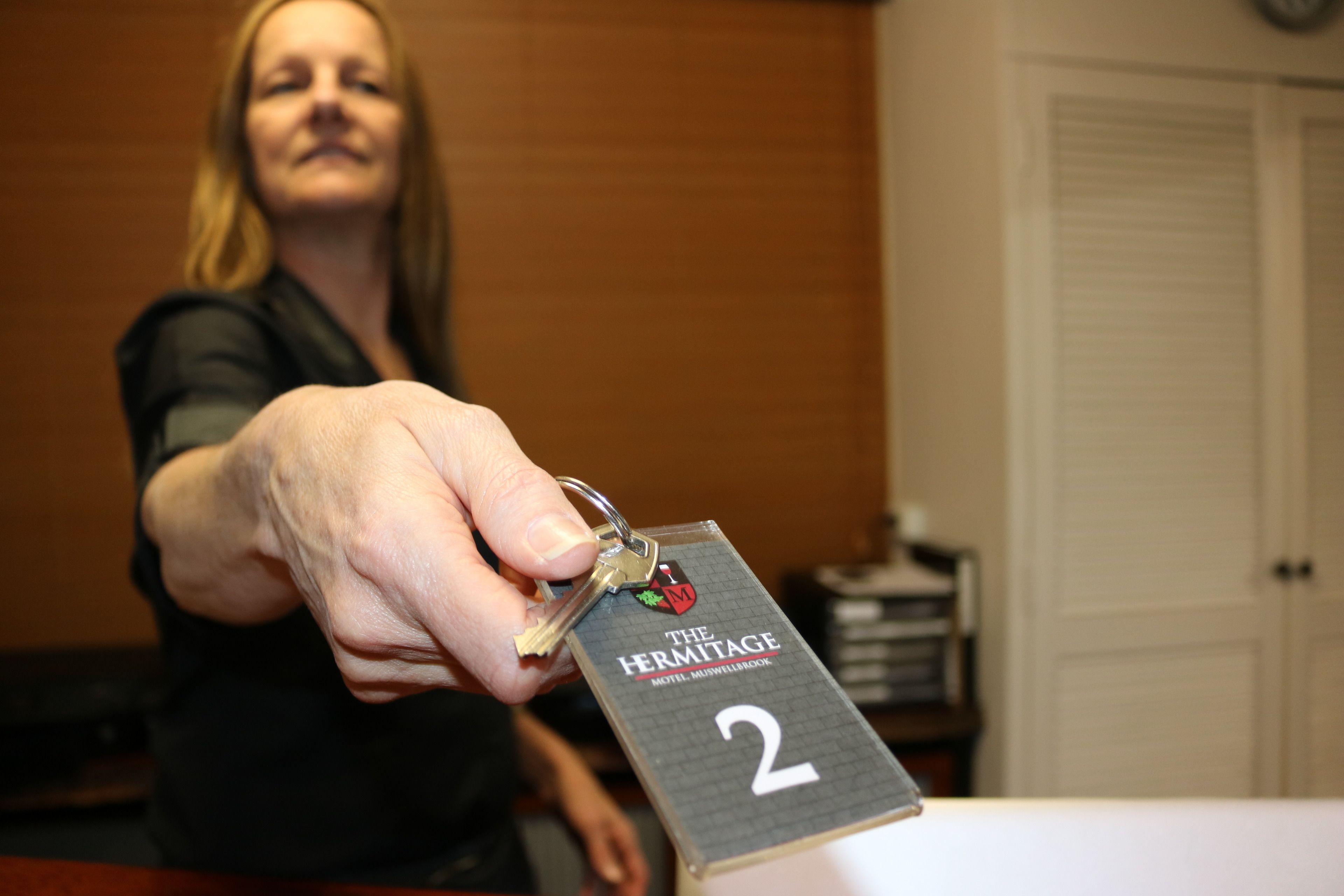A hand holding a key with a tag labeled "The Hermitage Motel - Marville Room 2".