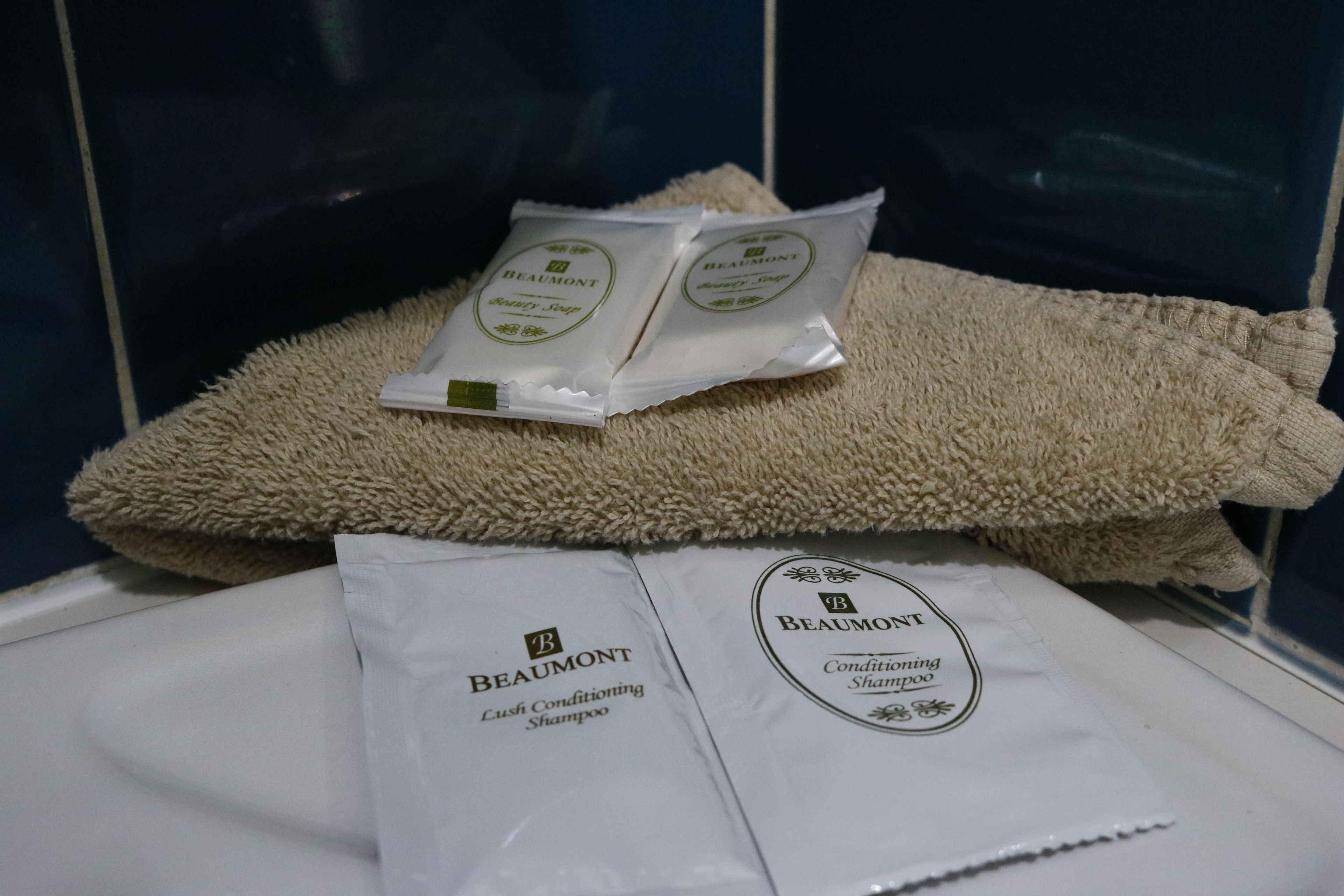 Two packages of Beaumont conditioning shampoo and a beige towel on a white surface.