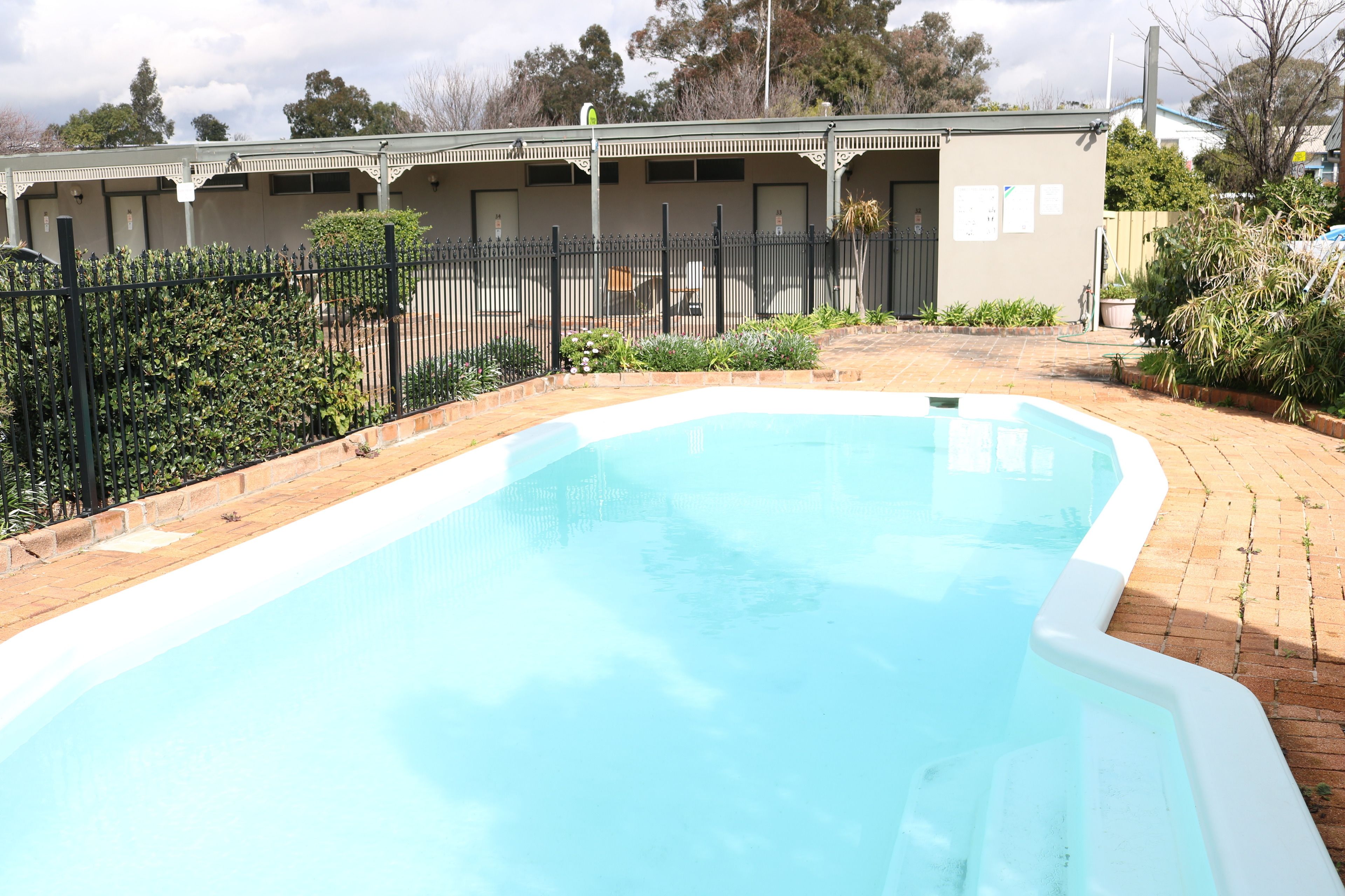 A swimming pool with a brick border, surrounded by a fence and greenery.