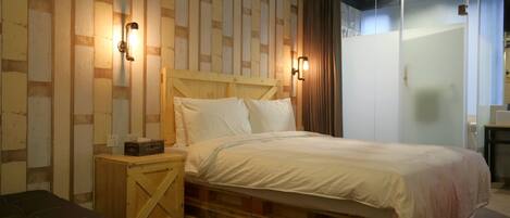 Une chambre à coucher avec une tête de lit en bois, un lit recouvert de draps blancs, une petite table de chevet en bois et un banc.