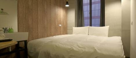 A bedroom with a wooden wall, a bed with white bedding, a bedside table, a mirror, and a window with curtains.
