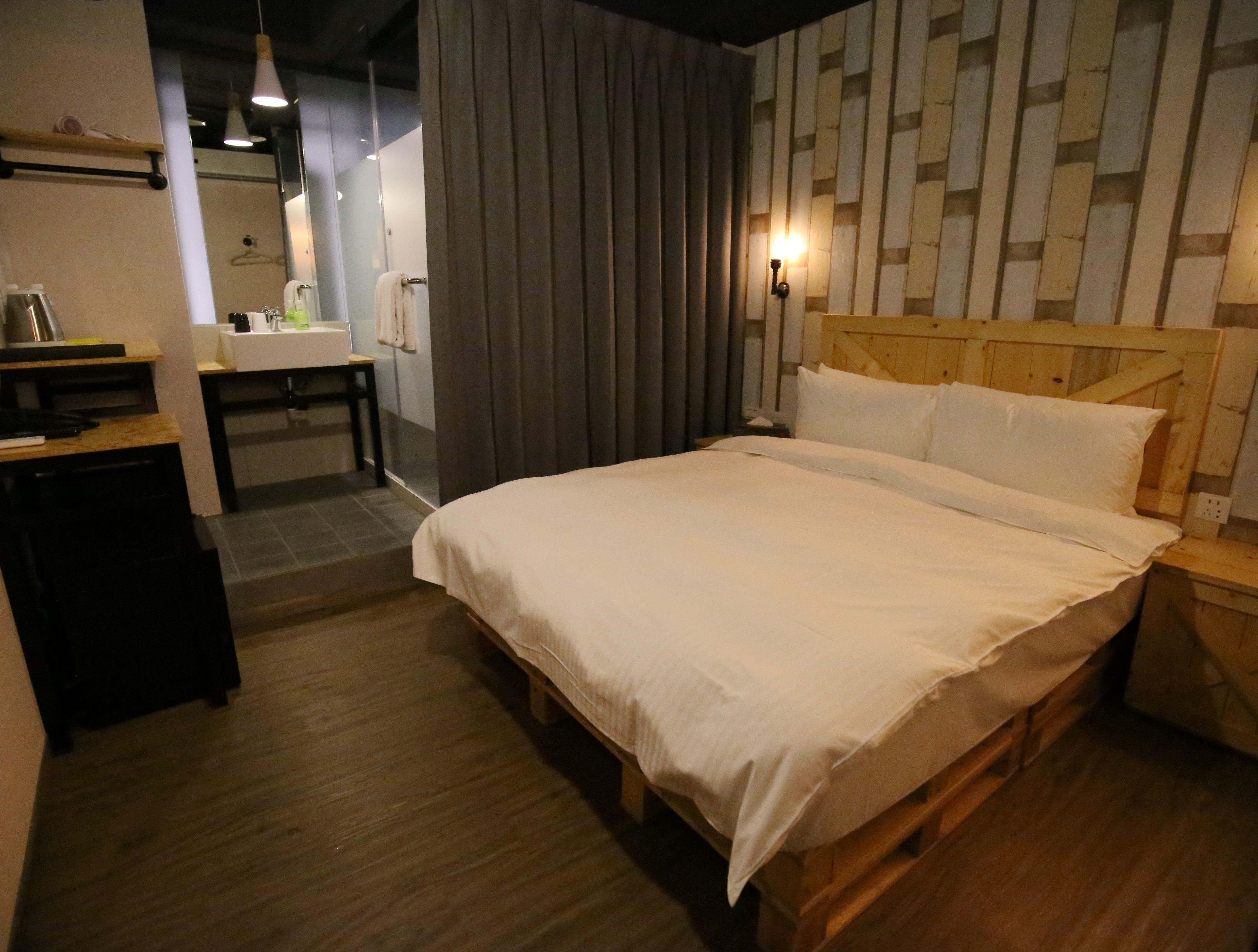 A bedroom with a wooden bed, a desk, and a bathroom visible in the background.