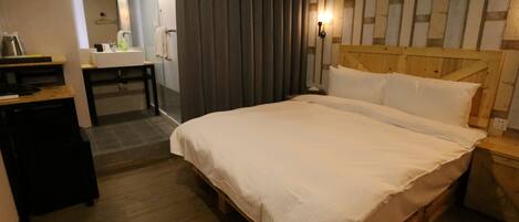 A bedroom with a wooden bed, a desk, and a bathroom visible in the background.