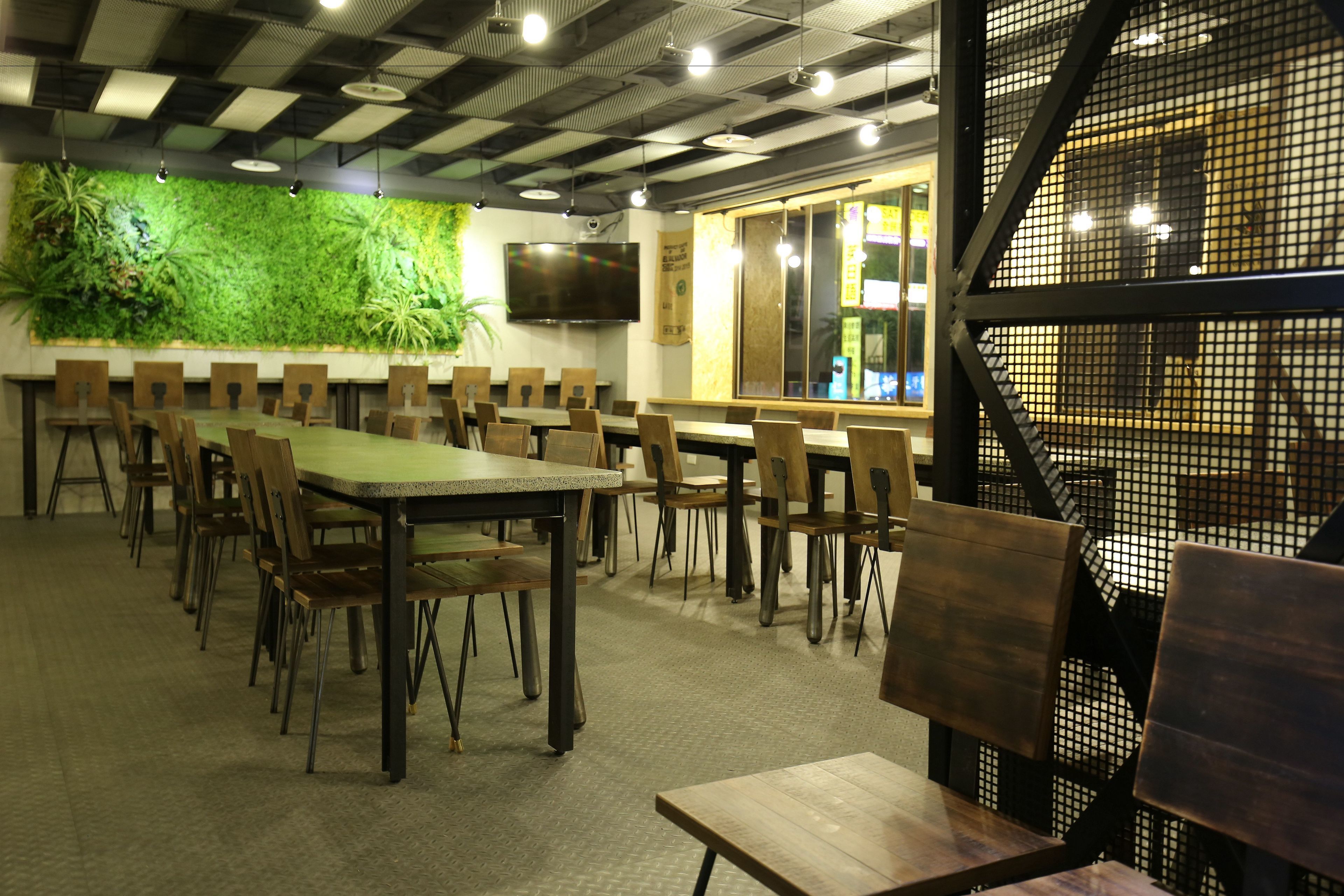 A conference room with long tables and chairs, a green wall with plants, a TV, and a window with a view.