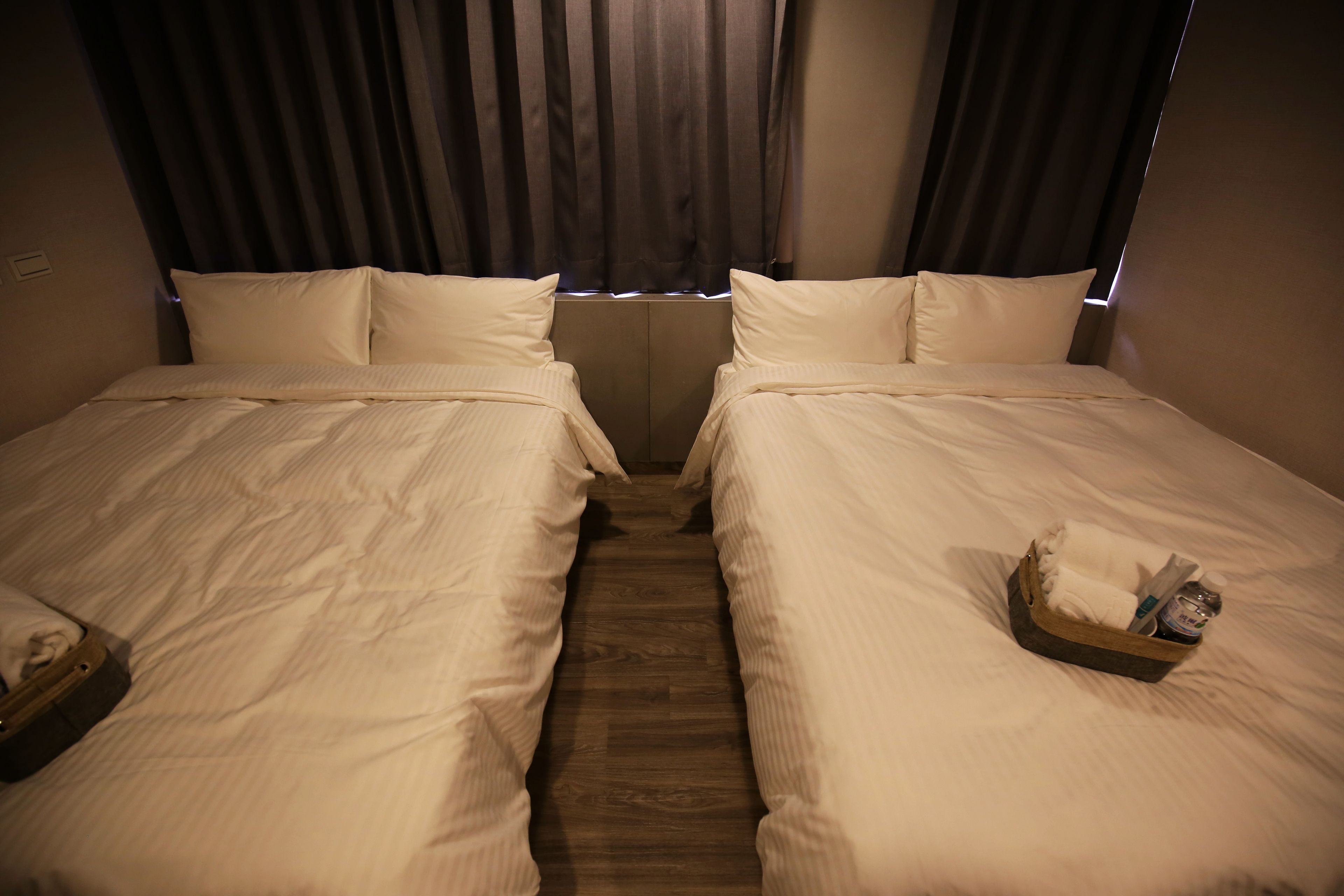 Een hotelkamer met twee bedden, een houten vloer en een raam met gordijnen.