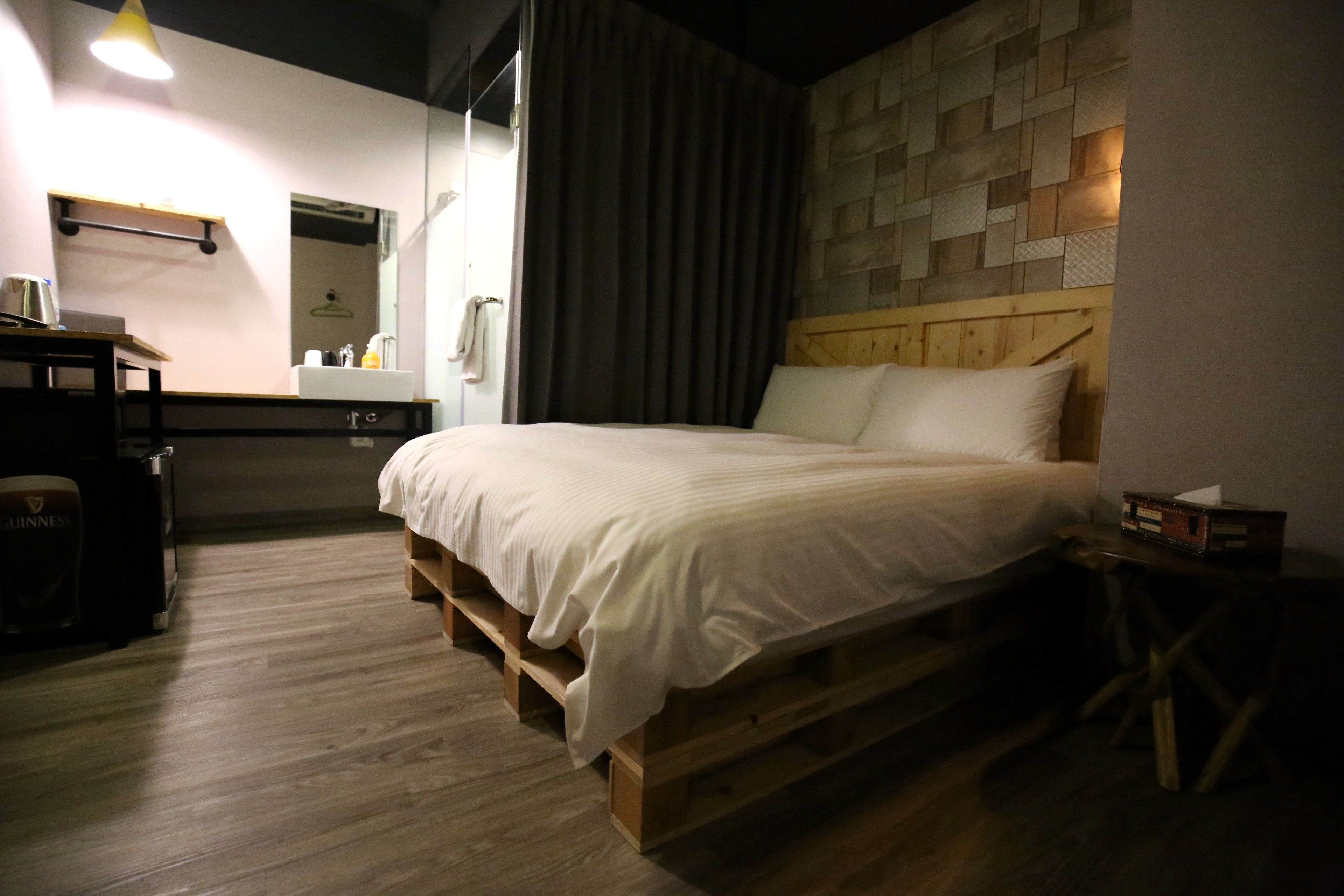 Une chambre à coucher bien rangée, avec un lit en bois, une petite table de chevet, un miroir, une étagère contenant des articles de toilette et un plancher en bois.