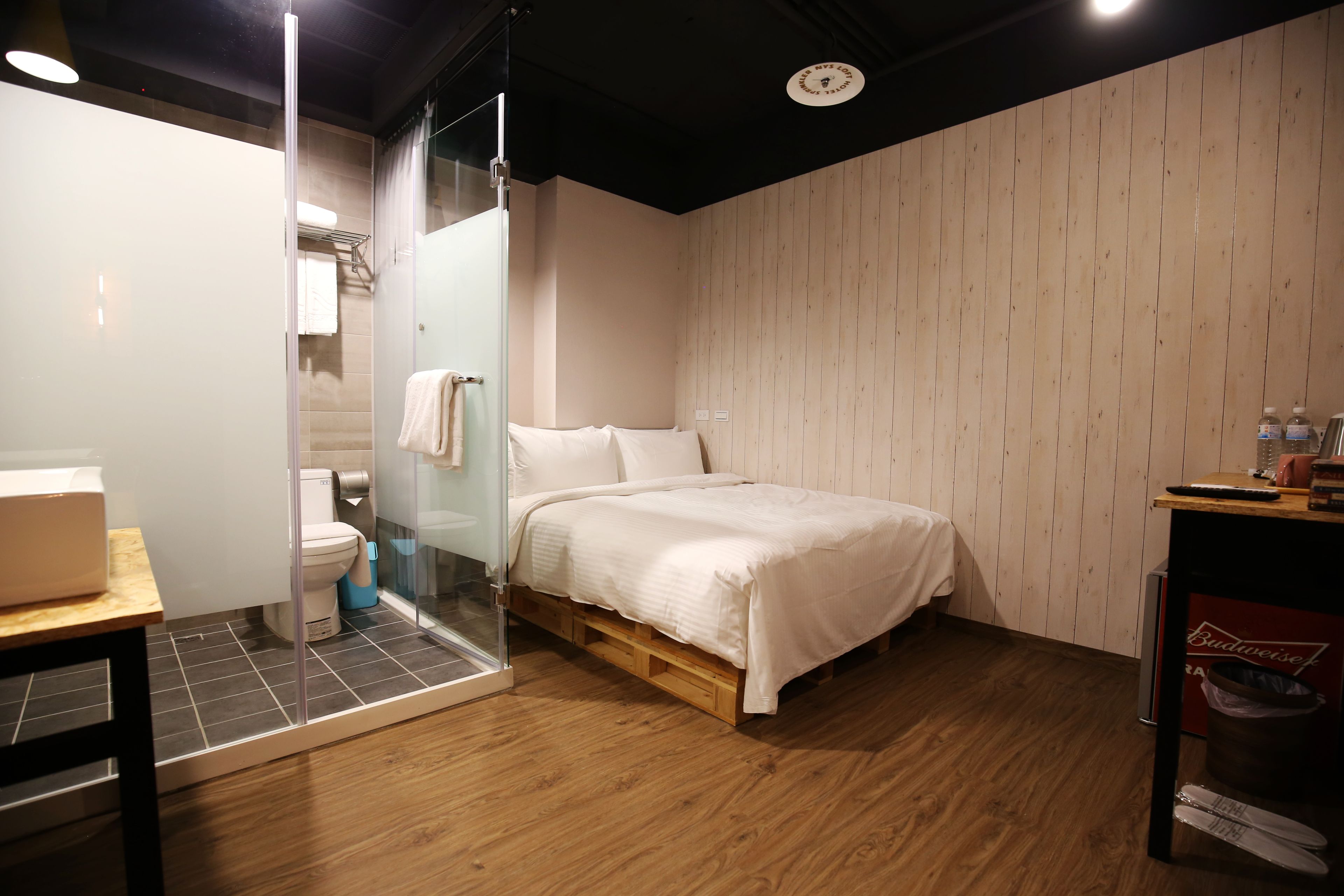 A modern bathroom with a glass shower enclosure, a toilet, and a bed with a wooden frame.