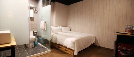 A modern bathroom with a glass shower enclosure, a toilet, and a bed with a wooden frame.