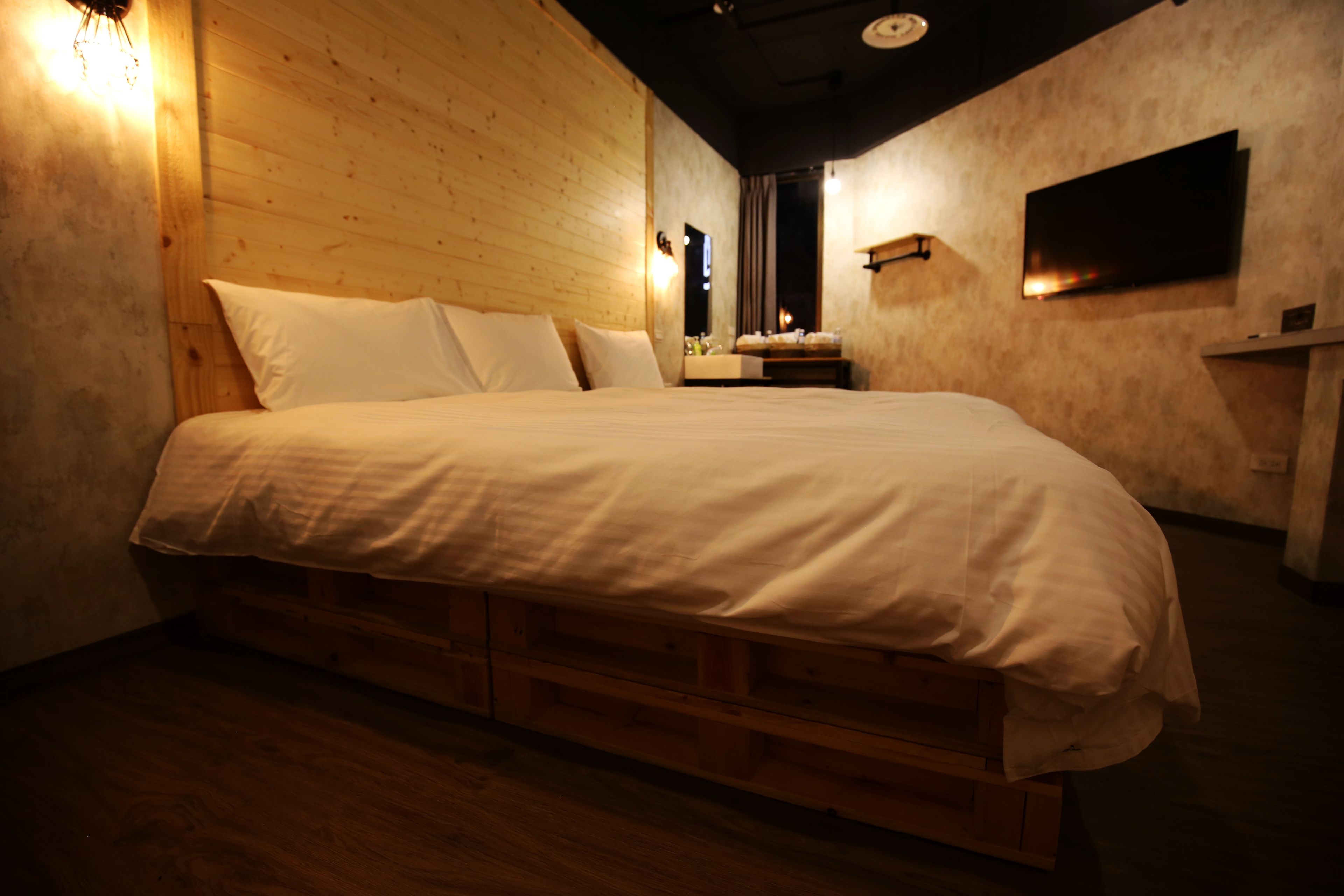 A large bed with a wooden headboard, a bedside table, and a mounted TV.