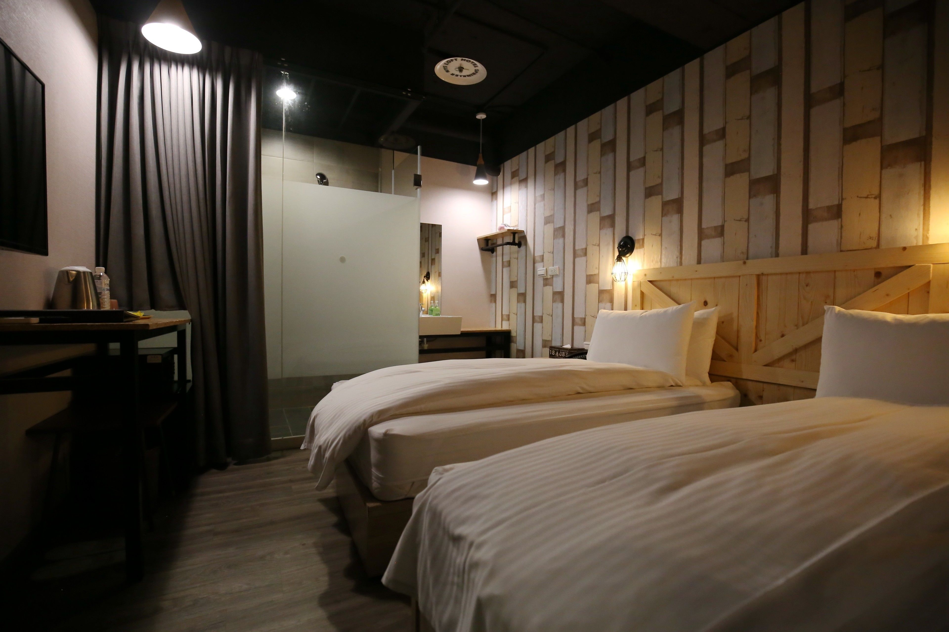 A hotel room with two beds, a wooden headboard, a desk with a chair, and a curtain.