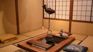 A tatami mat room with a traditional Japanese tea ceremony setup, including a tea kettle, a fish-shaped hanging ornament, and a small table with a teapot and cups. - Yuwaku Guesthouse - Hostel (Kanazawa)