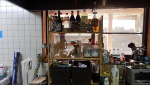 A kitchen with a window, shelves with bottles, and various kitchen utensils. - Yuwaku Guesthouse - Hostel (Kanazawa)