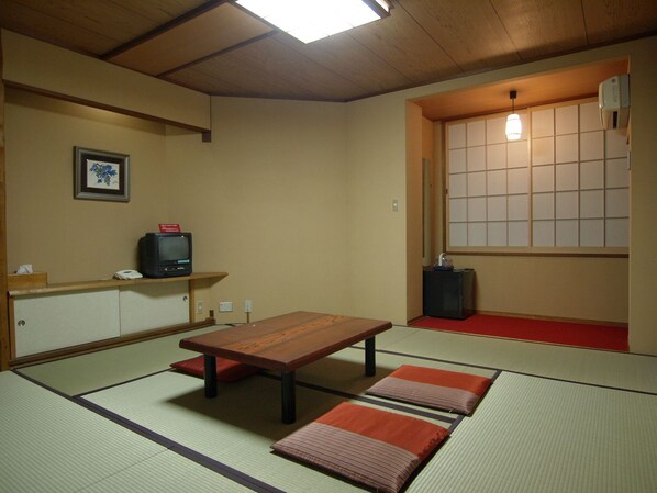 A tatami mat room with a wooden table, cushions, a television, and a sliding door with a view.