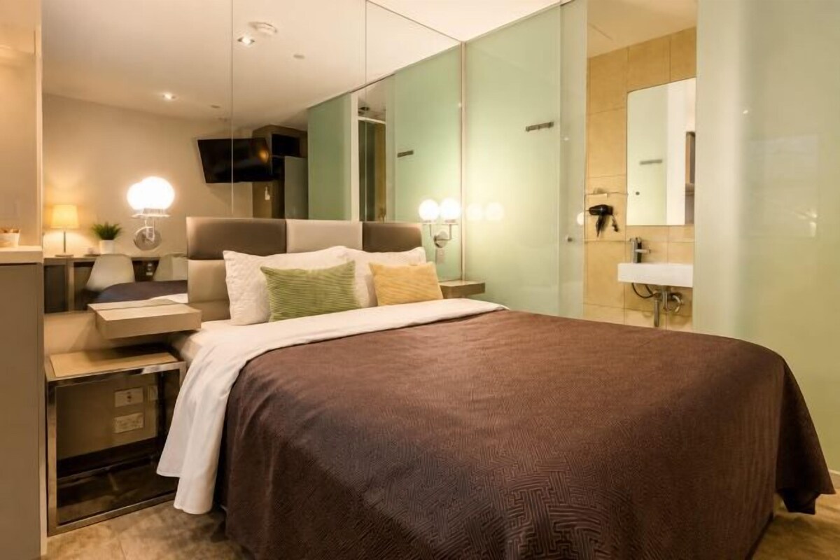 A modern bedroom with a large bed, bedside tables, a mirror, and a nightstand.