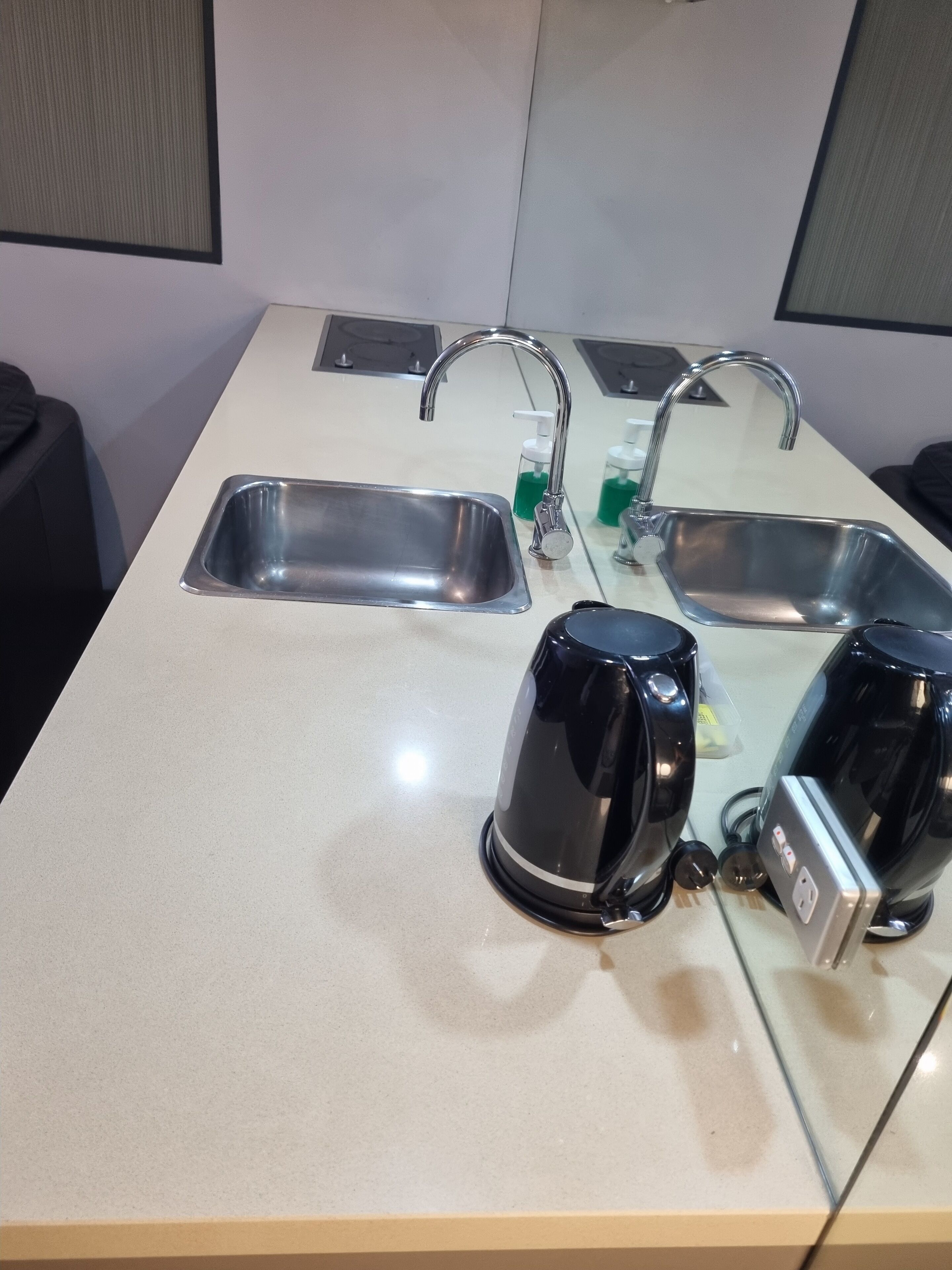 Una cocina con dos fregaderos de acero inoxidable, una tetera eléctrica negra y una cafetera.