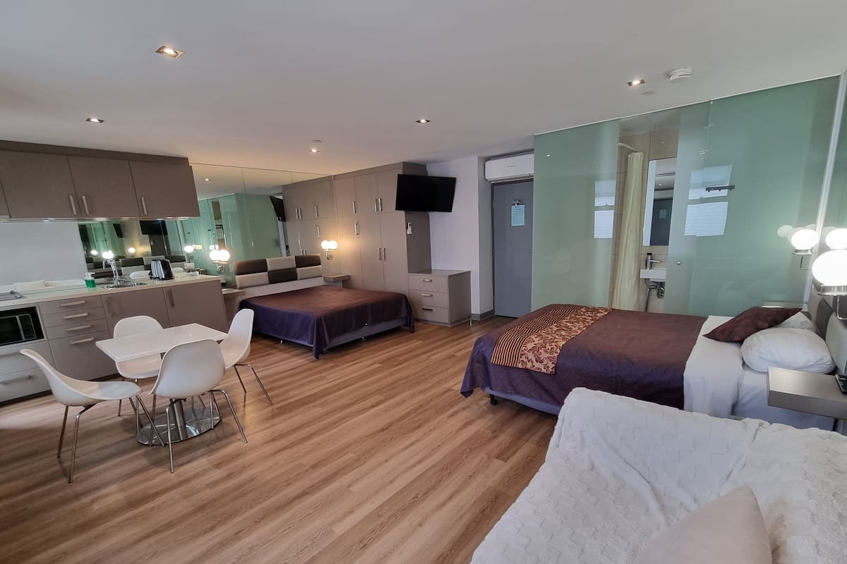 A modern hotel room with a bed, a sofa, a dining area, and a kitchenette.