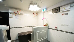 Baño con secamanos, un cubo de basura, un letrero de prohibido fumar y una flor sobre el mostrador.