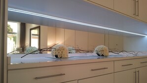 A modern kitchen with a long countertop, cabinets, and a large mirror above. - Fly Hotel (Luanda)