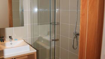 Ein modernes Badezimmer mit einer gläsernen Duschkabine, einem Holzbadezimmer-Möbel und einem Spiegel über dem Waschbecken.