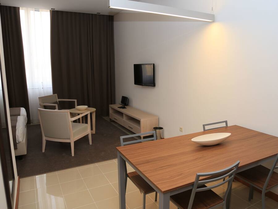 Una habitación de hotel moderna con una mesa de comedor de madera, dos sillas, un televisor pequeño y un sofá.