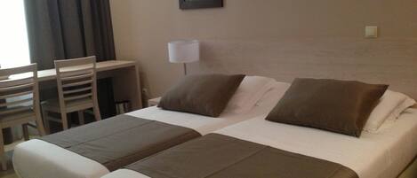 A hotel room with two beds, a desk, and a chair.