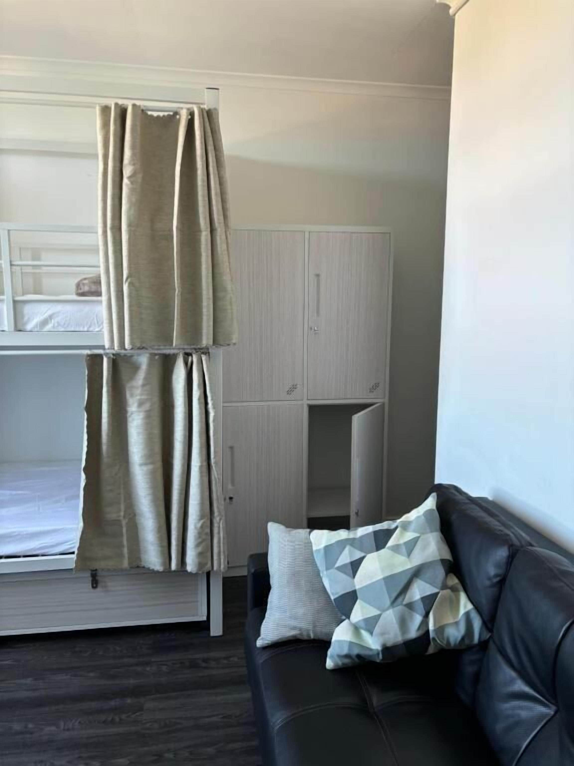 A room with a bunk bed, a wardrobe, a sofa with a patterned pillow, and a dark wooden floor.