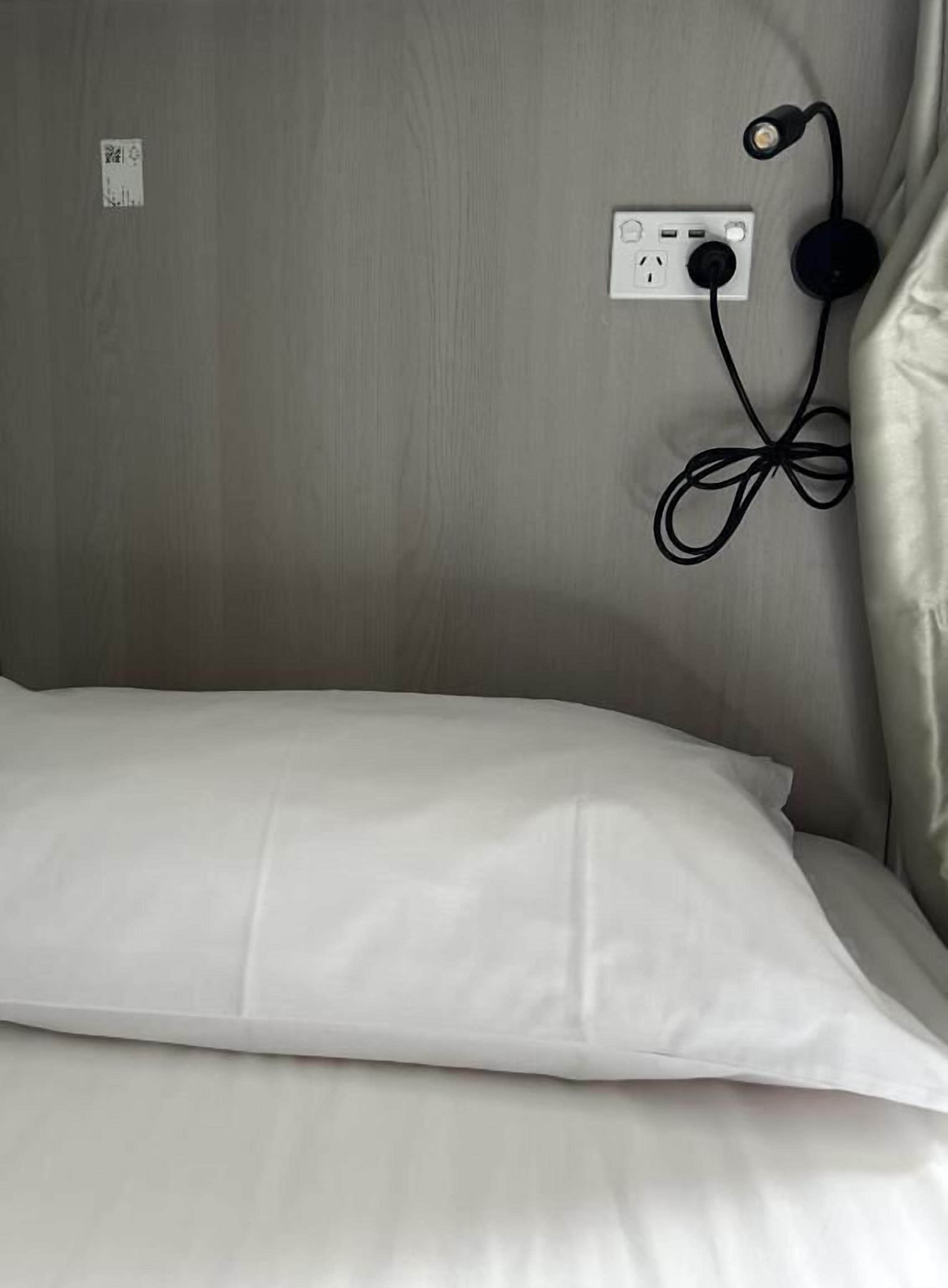 Een bed met een wit kussen en een stopcontact met een zwarte oplaadkabel.