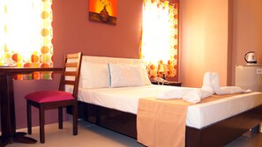 A hotel room with a bed, a desk, a chair, a nightstand, and a refrigerator. - Staylite Park B&B (Tagbilaran)