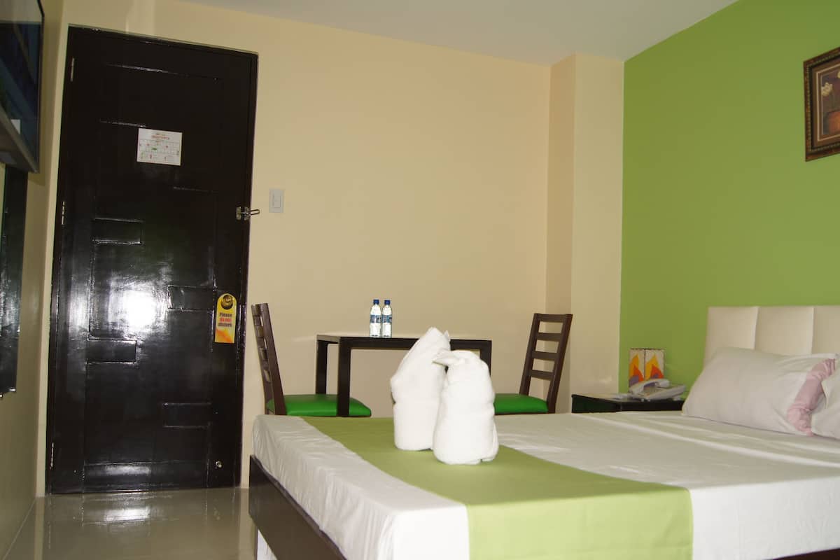 A hotel room with a bed, a green wall, a painting, a nightstand, and a door.