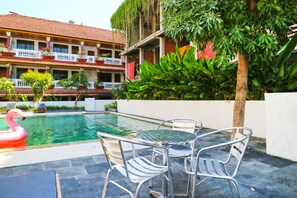 Una piscina con un galleggiante a forma di fenicottero, sedie in metallo e un edificio con balconi e piante in vaso.