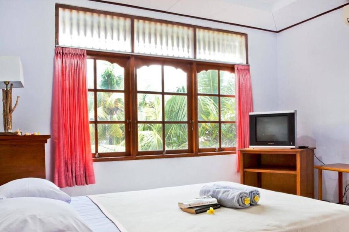 Une chambre d’hôtel avec un lit, un téléviseur posé sur un meuble en bois et une fenêtre avec des rideaux.