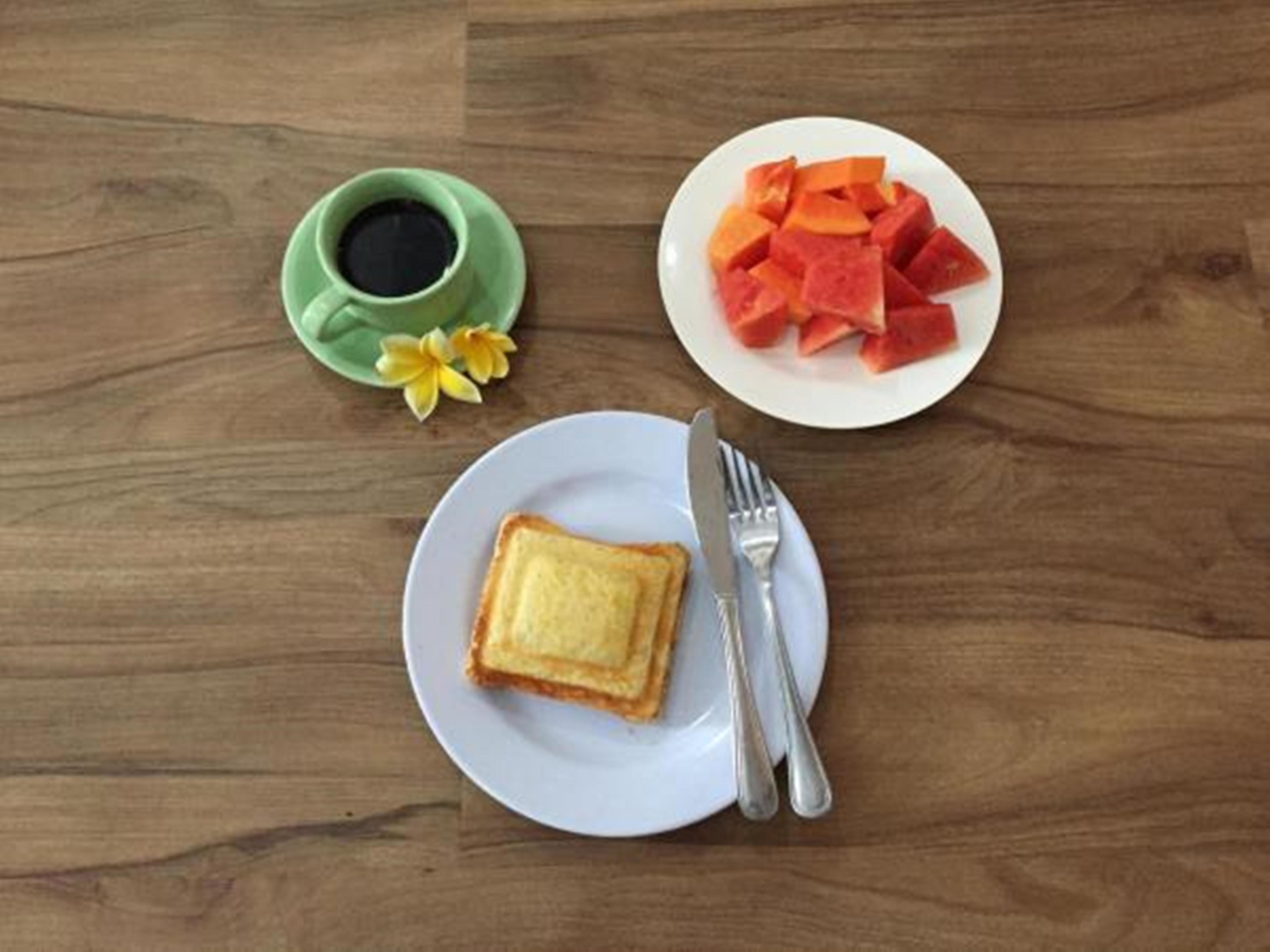 A wooden table with a plate of toast, a plate of watermelon, and a green cup with a flower.