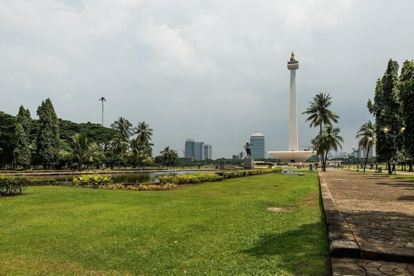 Un parque con un monumento alto, un estanque y un paisaje urbano al fondo.