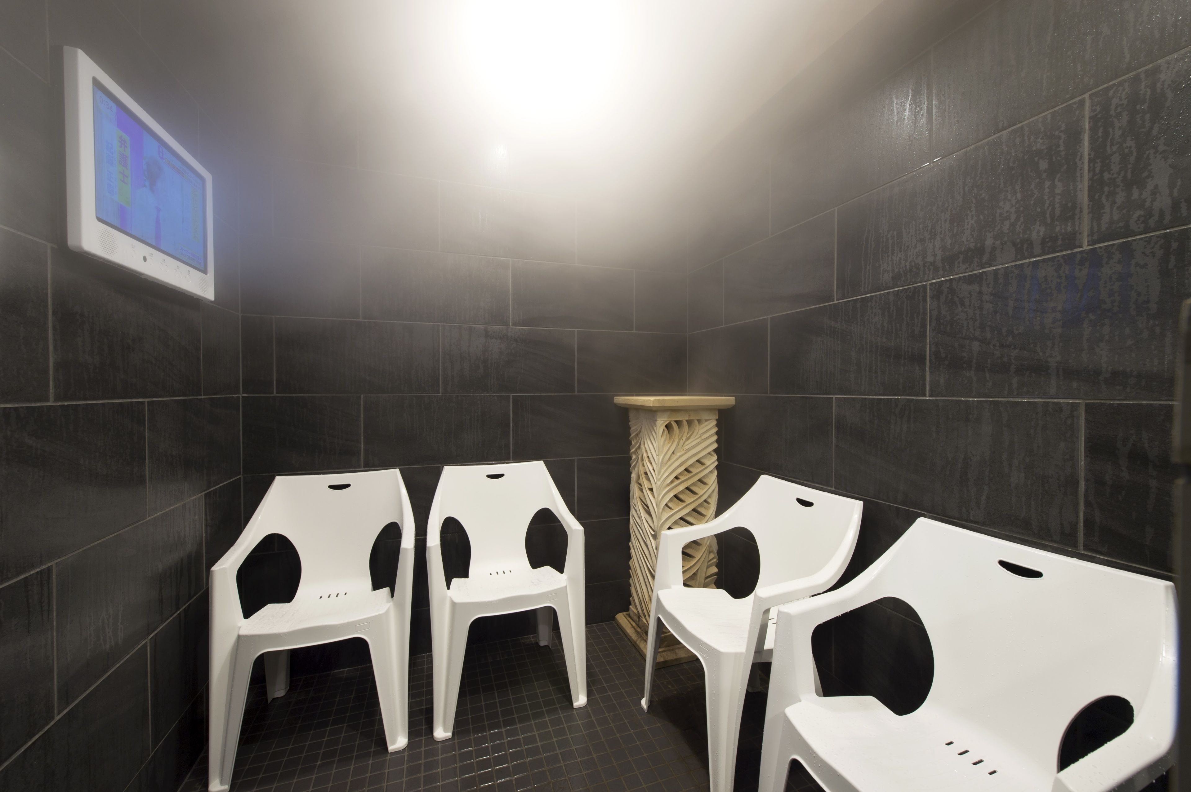 Des toilettes aux murs recouverts de carreaux sombres, avec des cuvettes blanches et un écran affichant une interface bleue.