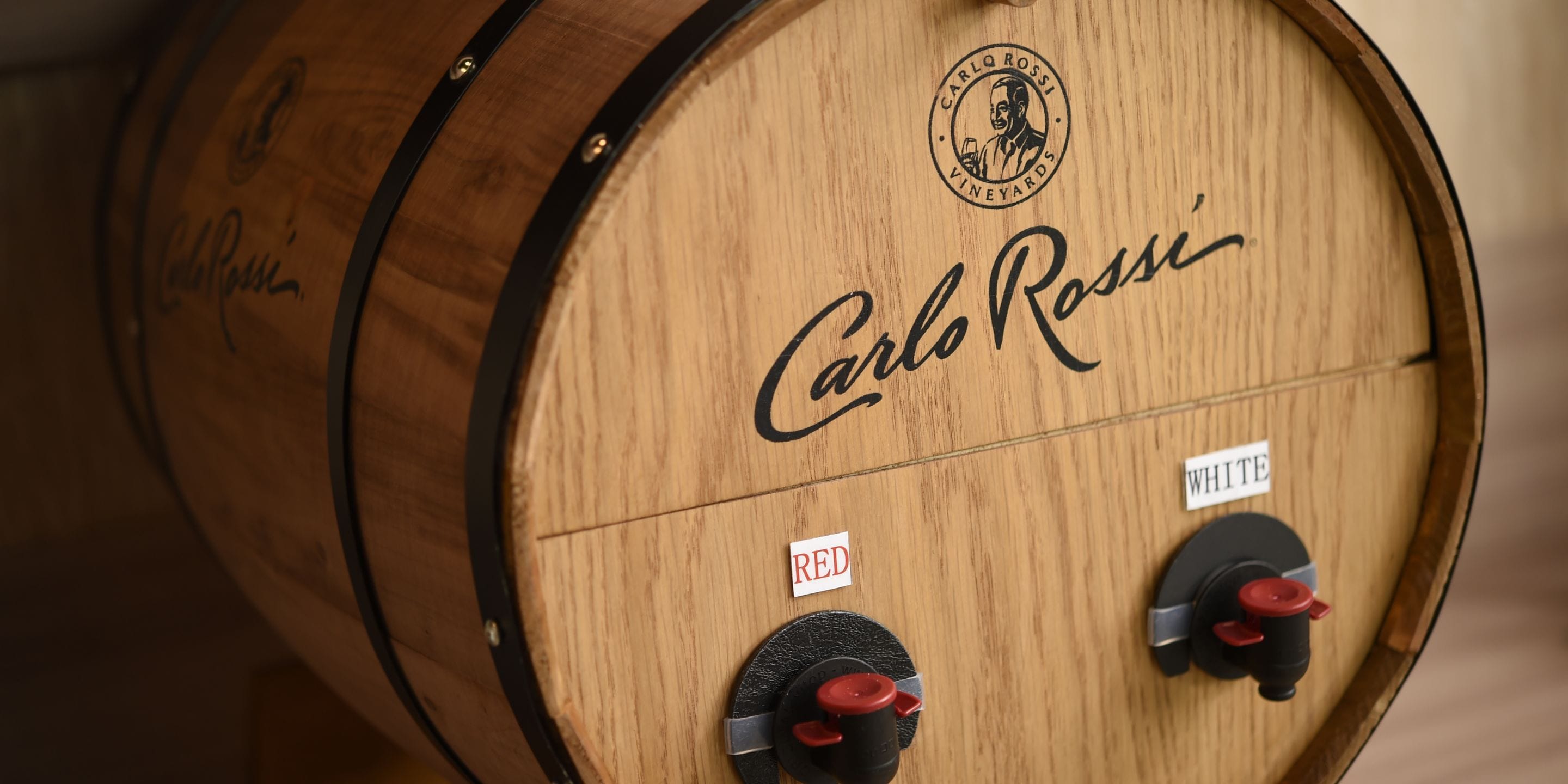 Un barril de madera con el nombre 'Carlo Rossi' y dos manijas de grifo etiquetadas como 'REDO' y 'BLANCO'.