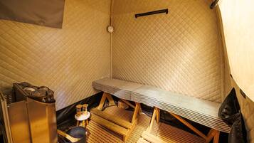 A small, cozy room with a quilted wall, a wooden bench, a small table with a kettle, and a heater.
