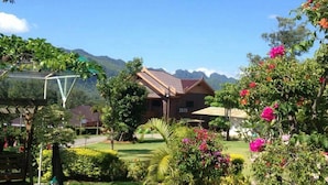 A traditional wooden house with a tiled roof, surrounded by lush greenery and flowering plants.