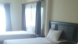 Two single beds with wooden frames and white bedding in a room with wooden flooring and a plain white wall.