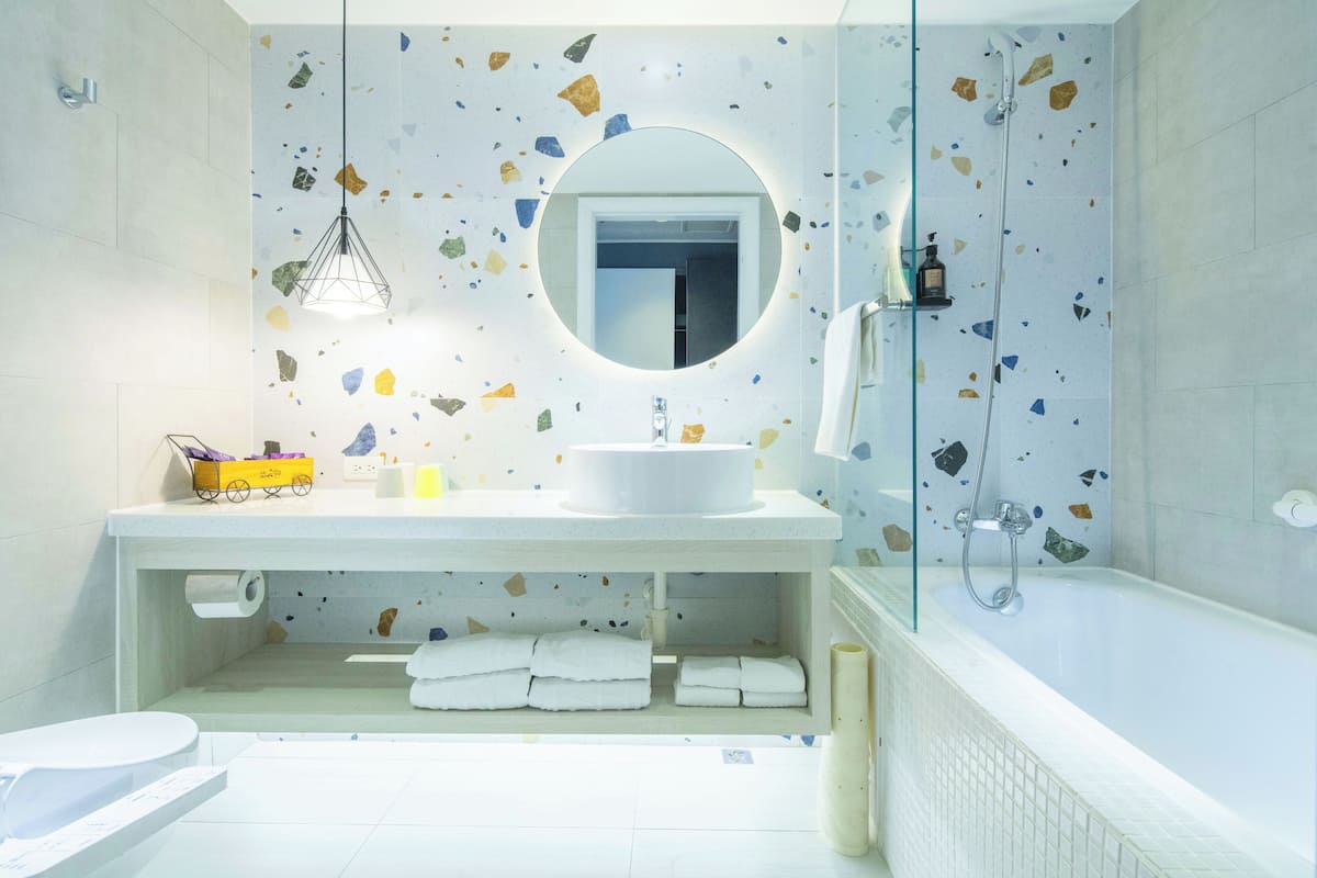 A modern bathroom with a round mirror, white sink, and a glass-enclosed shower.