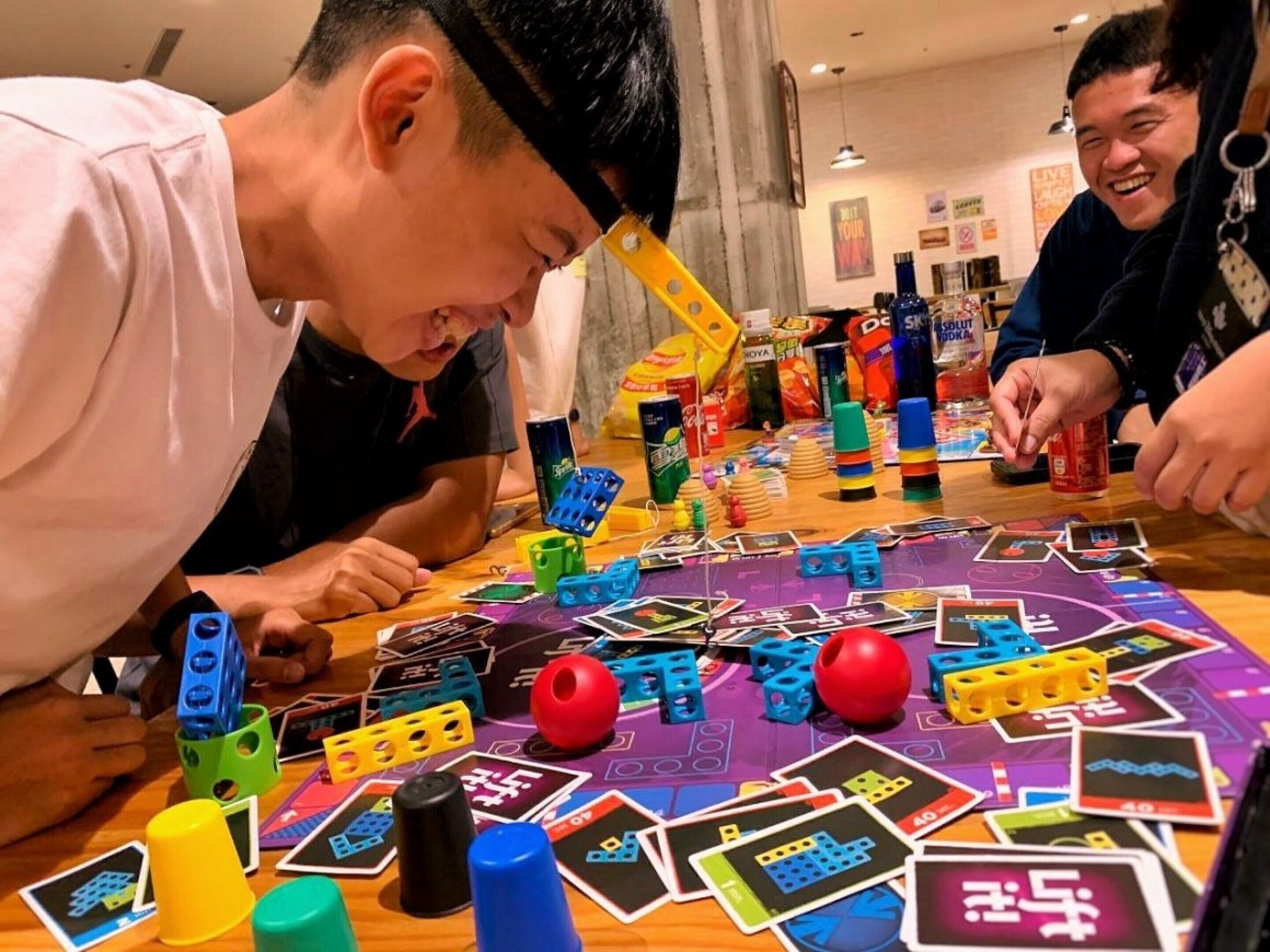 Un groupe de personnes joue à un jeu de société sur une table, en utilisant des pièces et des cartes aux couleurs vives.