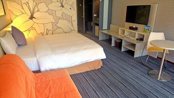 A hotel room with a large bed, a sofa, a TV, a desk, and a chair.
