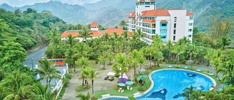 A resort with a large swimming pool surrounded by palm trees and a mountain backdrop.