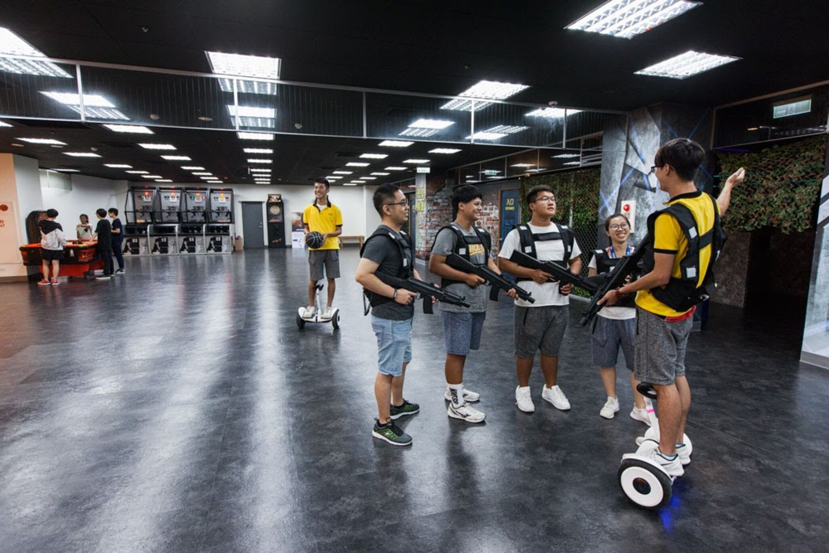 A group of people on hoverboards in a spacious indoor area with a polished floor and modern lighting.