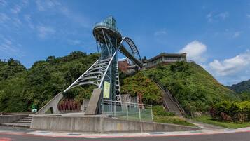 A modern architectural structure with a glass and metal design, surrounded by lush greenery and a clear blue sky.